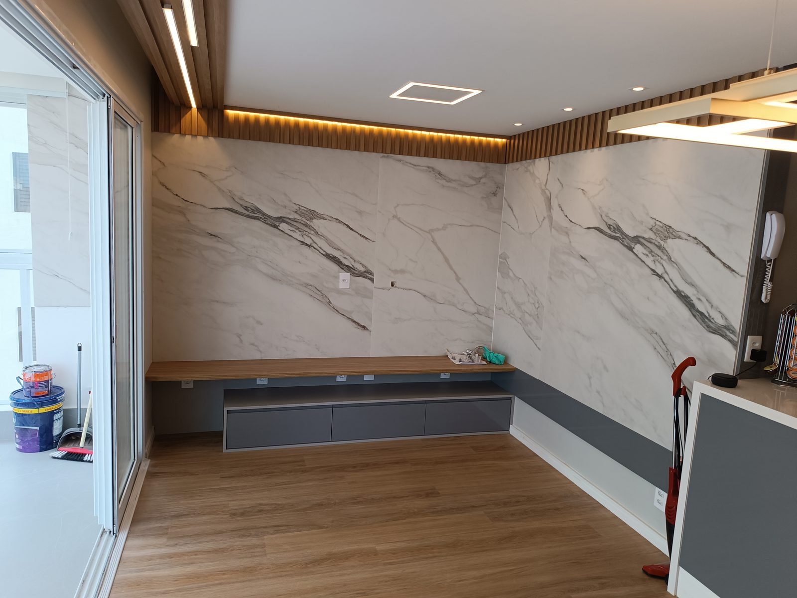 Depois da reforma: living concluído com painel de porcelanato marmorizado, ripado de madeira, bancada suspensa e iluminação LED